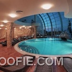 Fabulous Rounded Indoor Swimming Pool Design with Rattan Lounge Chairs